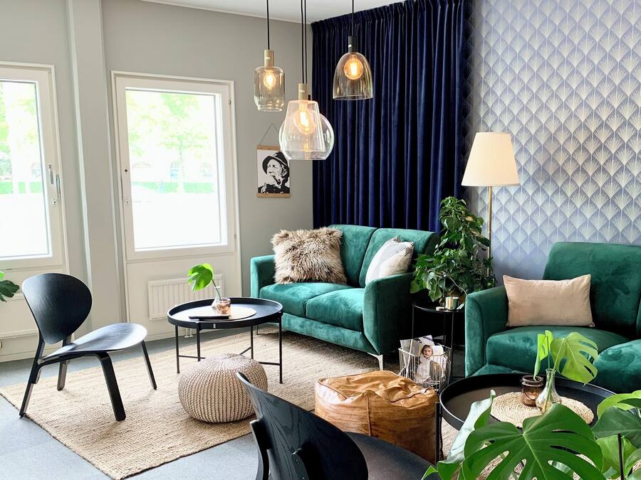 Un salon moderne avec un canapé vert, un fauteuil noir, une petite table ronde et des lampes suspendues.