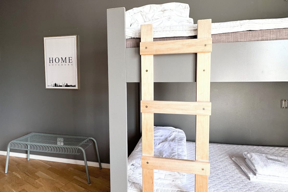Ein Stockbett mit einer Holzleiter, einer kleinen Bank und einem gerahmten Schild an der Wand.