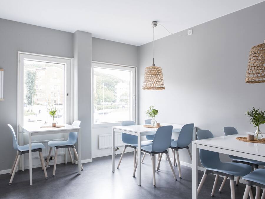 Un comedor moderno con una mesa blanca y sillas azules, ventanas amplias y una lámpara colgante de mimbre.