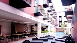A modern indoor atrium with a pool area, multiple dining tables, and lounge seating. - Amaris Hotel Pratama Nusa Dua (Nusa Dua)