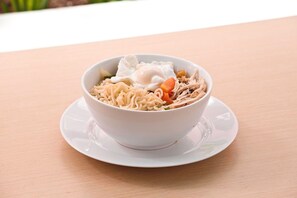 A bowl of ramen with noodles, vegetables, and a poached egg on a white plate. - Amaris Hotel Pratama Nusa Dua (Nusa Dua)