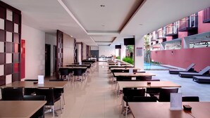A modern dining area with long tables and chairs, a reception desk, and a poolside area with lounge chairs. - Amaris Hotel Pratama Nusa Dua (Nusa Dua)