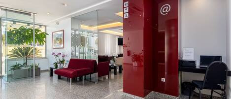 A modern reception area with a red desk, black chairs, and a glass partition.