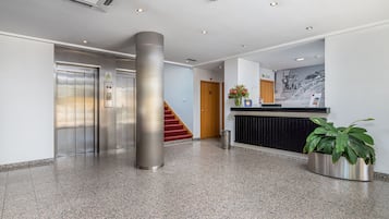 Un vestíbulo moderno con una recepción, un pilar grande, un ascensor y una escalera.