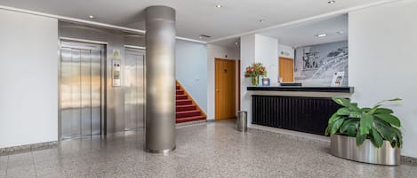 Un vestíbulo moderno con una recepción, un pilar grande, un ascensor y una escalera.
