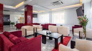 A modern hotel lobby with red and beige sofas, a central table, and a large window with curtains. - Stay Hotel Leiria Centro (Leiria)