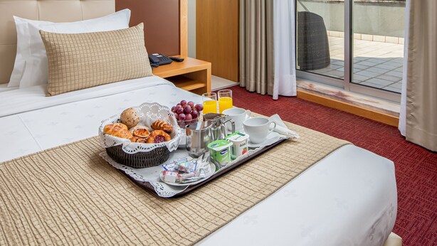 A hotel room with a bed, a tray of breakfast items, a nightstand, and a large window with a city view. - Stay Hotel Leiria Centro (Leiria)