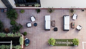 An outdoor seating area with multiple lounge chairs and tables, surrounded by potted plants and a sign reading "KHRONOS BCN". - Hostal Boutique Khronos (Barcelona)
