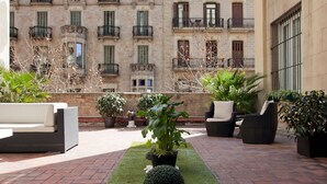 A rooftop patio with outdoor furniture, potted plants, and a view of a building with balconies. - Hostal Boutique Khronos (Barcelona)