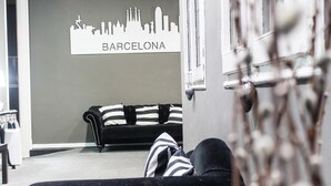 A living room with a black and white striped sofa, a city skyline silhouette on the wall, and a window with a view. - Hostal Boutique Khronos (Barcelona)