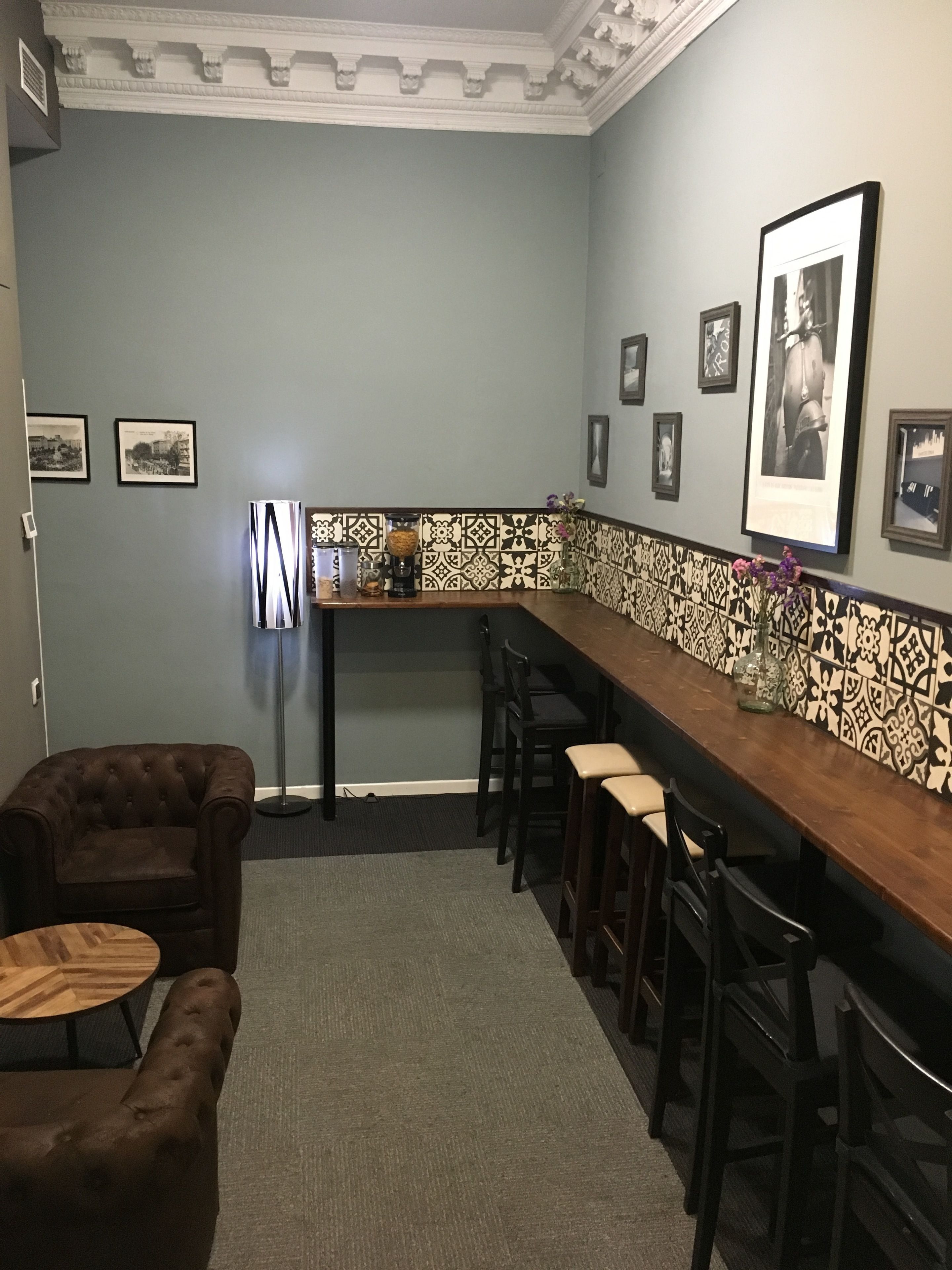 Un espace bar doté d’un long comptoir en bois, de plusieurs tabourets et de tableaux encadrés accrochés au mur.