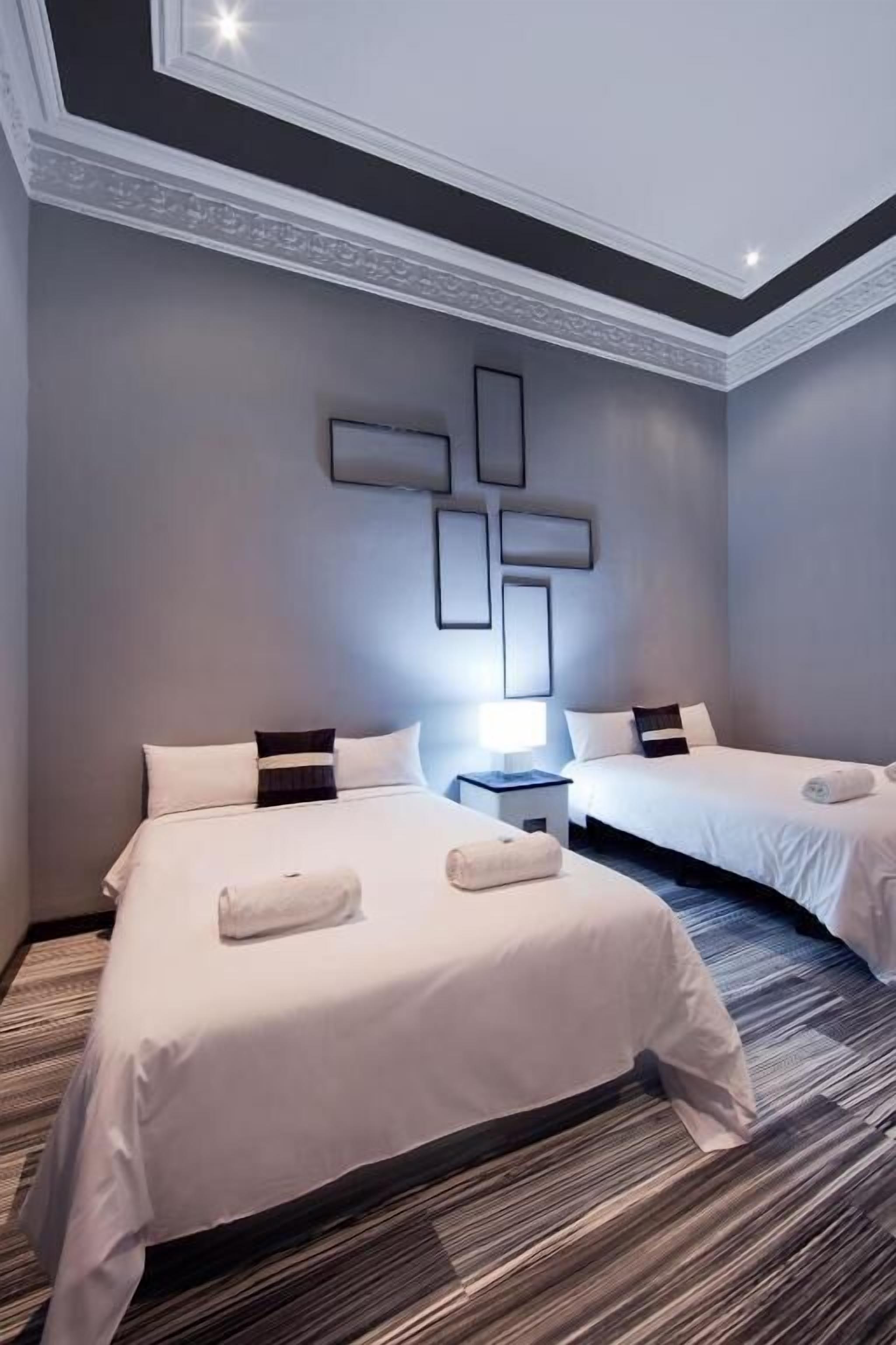 A hotel room with two beds, a modern ceiling design, and a decorative wall piece.