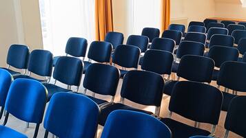 Rijen blauwe stoelen gerangschikt in een congreszaal met een schuine plafond en grote ramen voorzien van gordijnen.