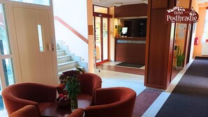Un vestíbulo de hotel con una recepción, una escalera y una zona de estar con una mesa y sillas.