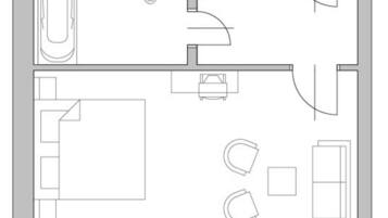 A floor plan of a hotel room with a bathroom, a small sitting area, a bed, and a desk.