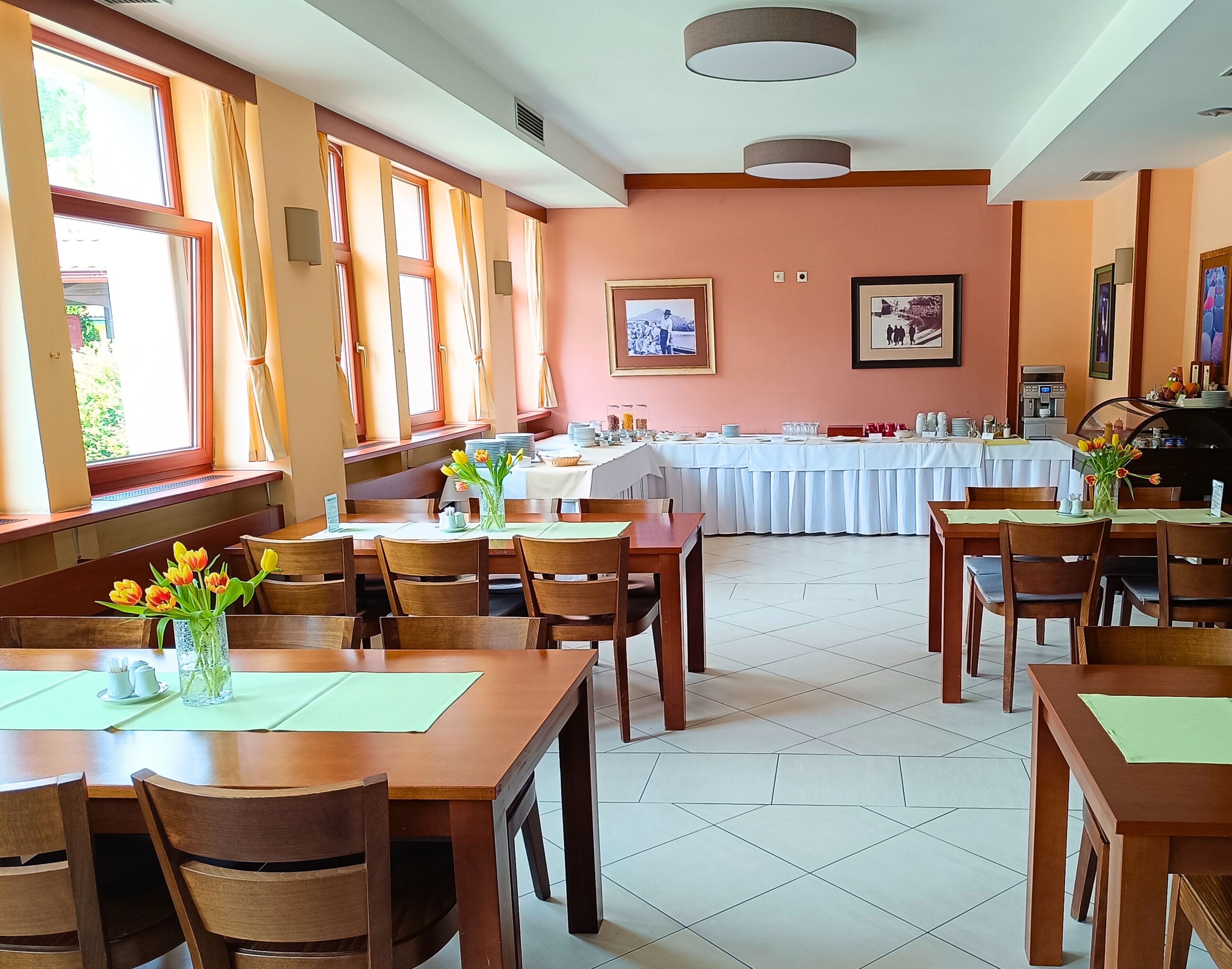 A dining area with wooden tables and chairs, a buffet setup, and large windows with curtains.