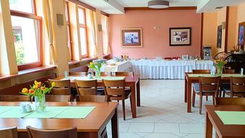 A dining area with wooden tables and chairs, a buffet setup, and large windows with curtains.