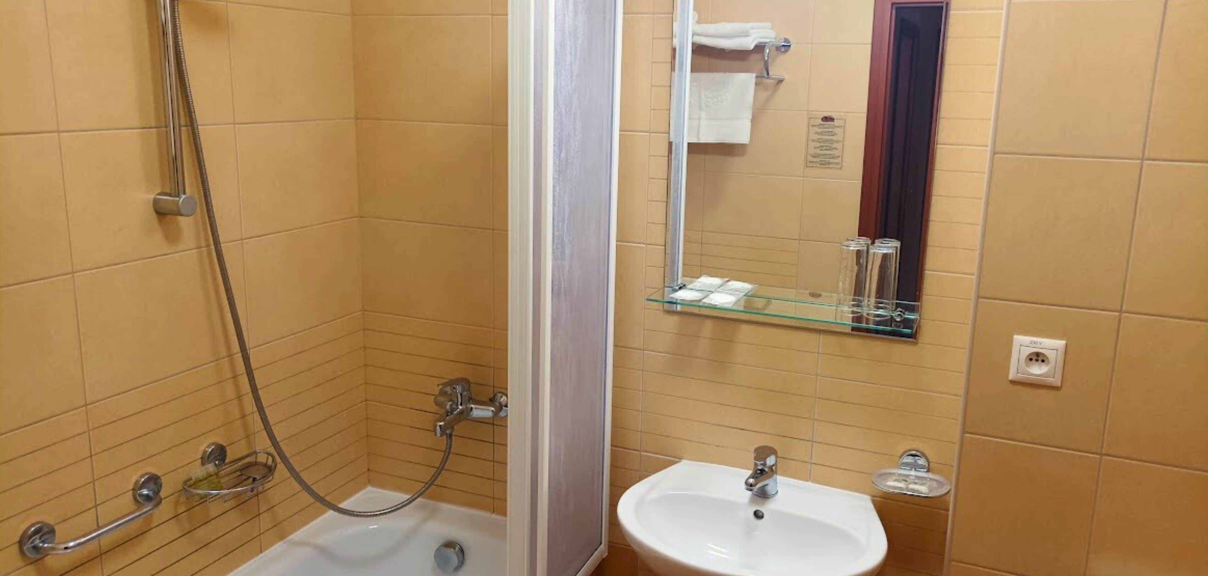 A bathroom with a shower, a sink, and a glass shelf with toiletries.