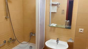 A bathroom with a shower, a sink, and a glass shelf with toiletries.