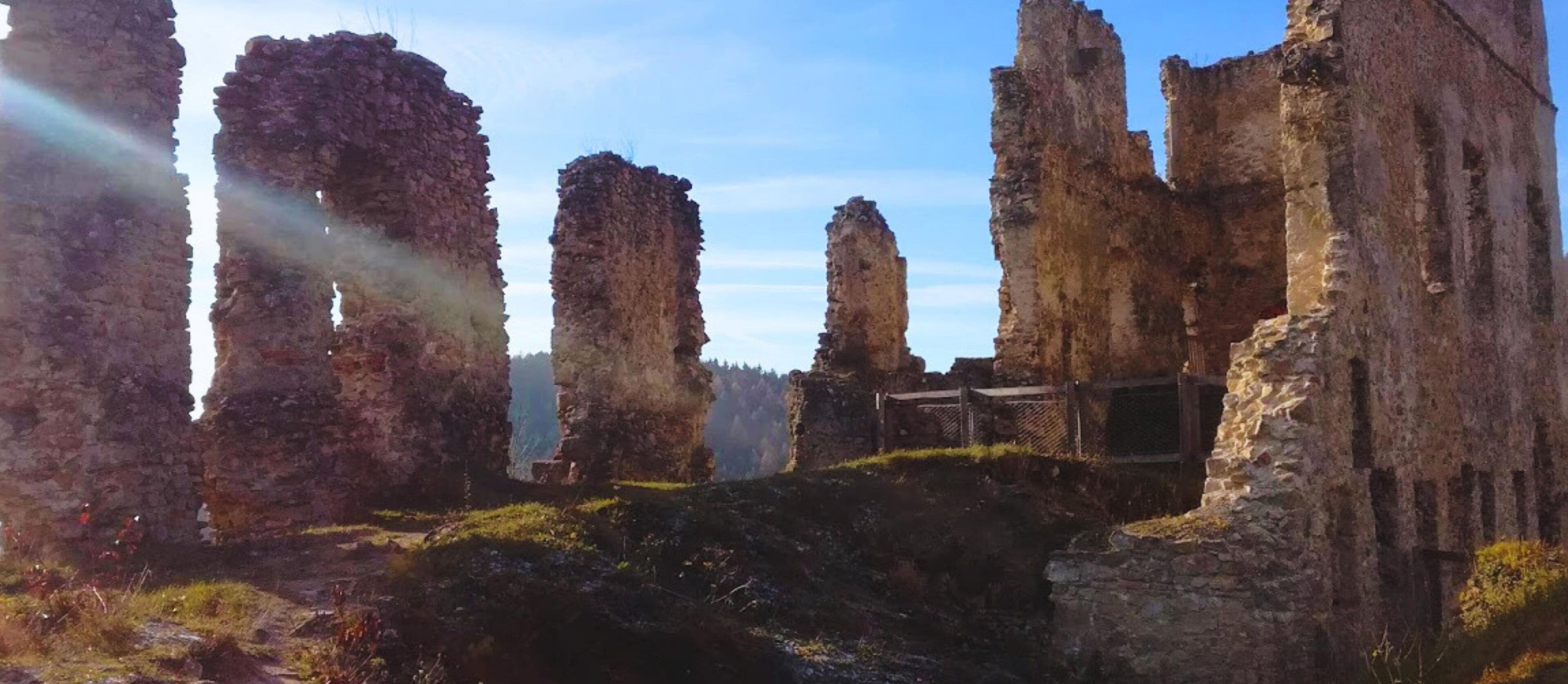 Vestiges d’une ancienne construction en pierre, avec de hauts murs érodés par le temps et un parterre d’herbe au premier plan.