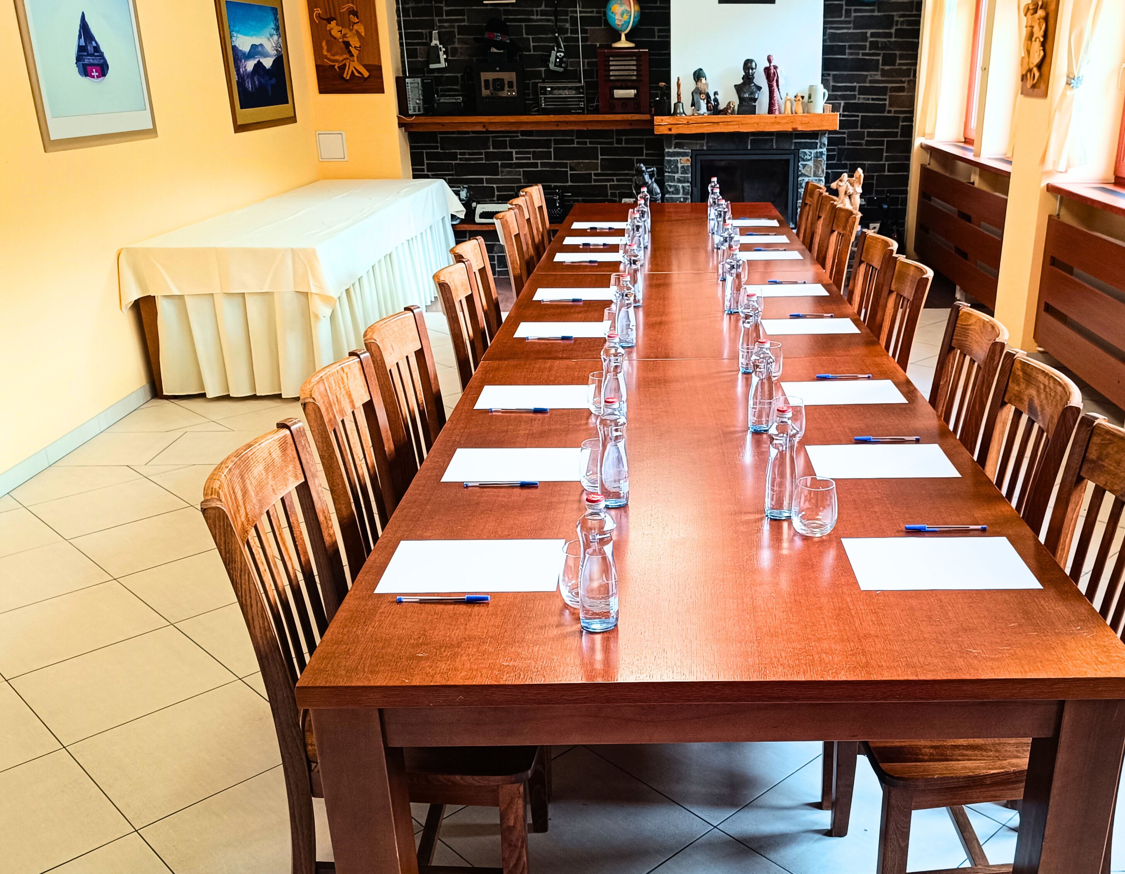 Una larga mesa de conferencias de madera con sillas, manteles blancos y cristalería transparente.
