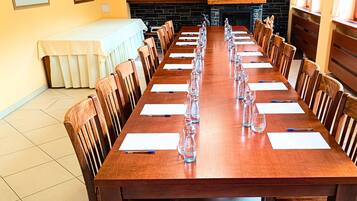 Una larga mesa de conferencias de madera con sillas, manteles blancos y cristalería transparente.