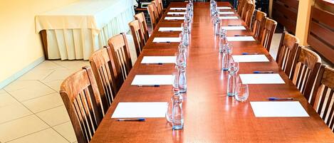 A long wooden conference table with chairs, white tablecloths, and clear glassware.