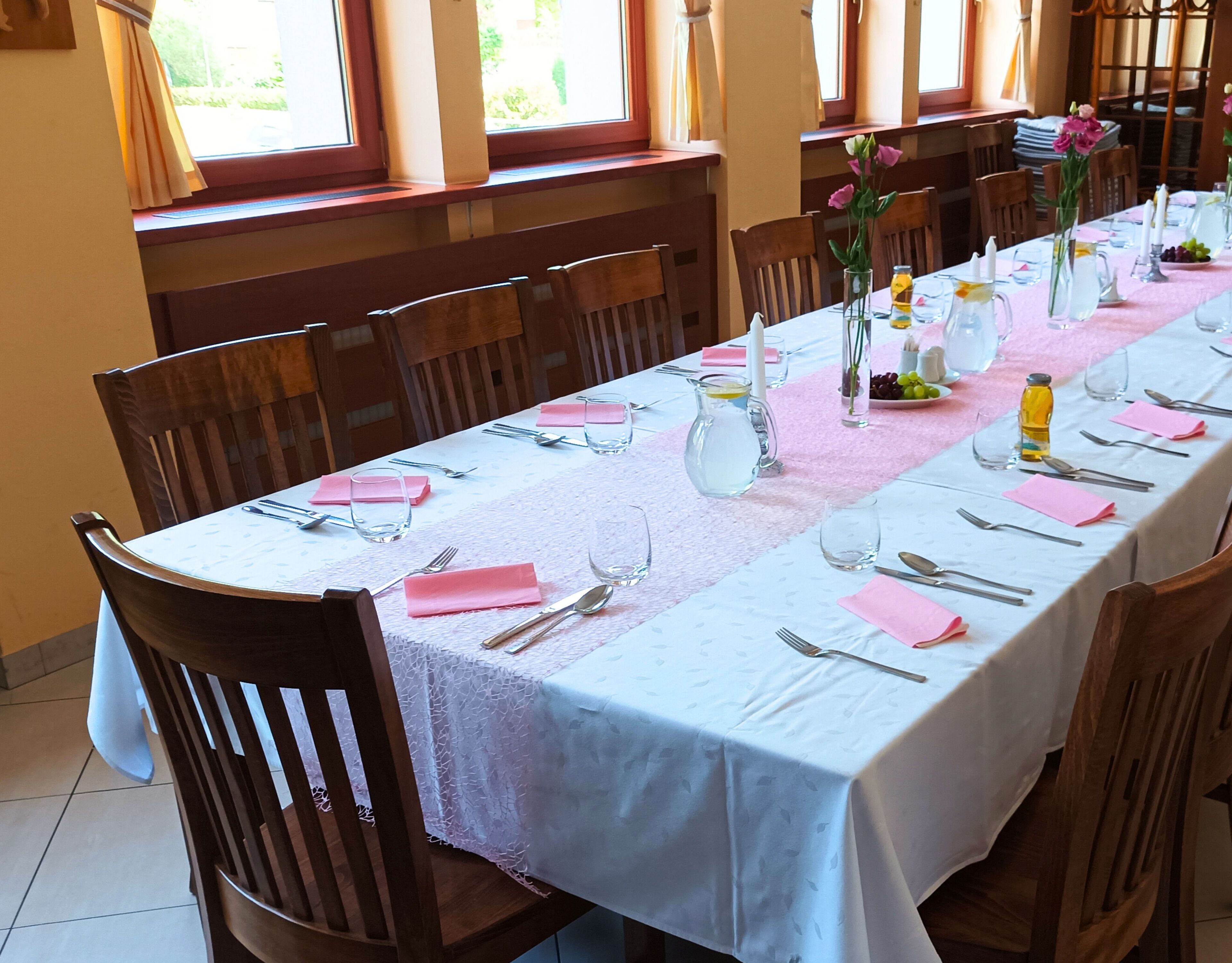 A long dining table set for a meal with chairs around it, a pitcher, and a vase with flowers.