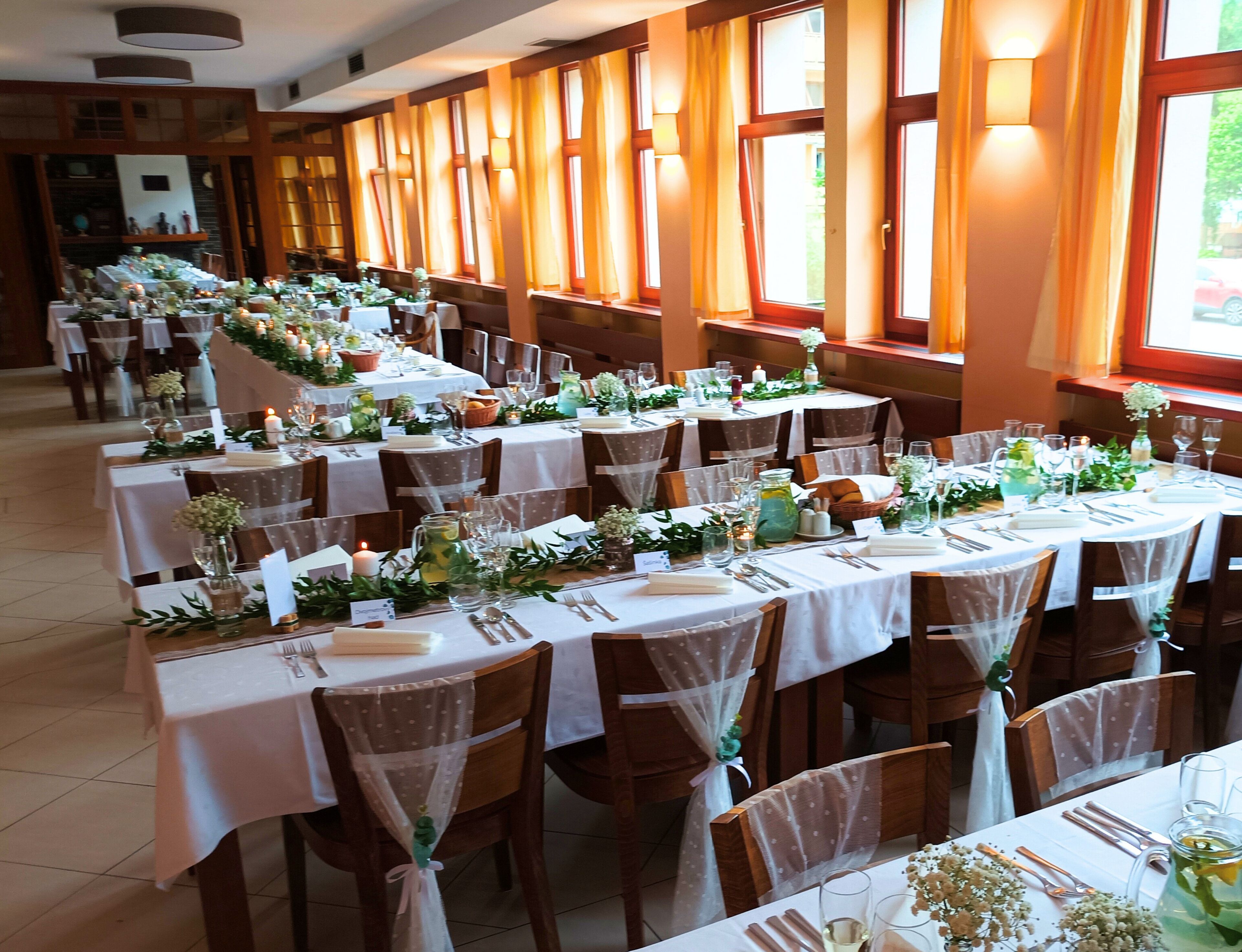 A banquet hall with multiple round tables set for a formal event, featuring white tablecloths, floral centerpieces, and neatly arranged cutlery.