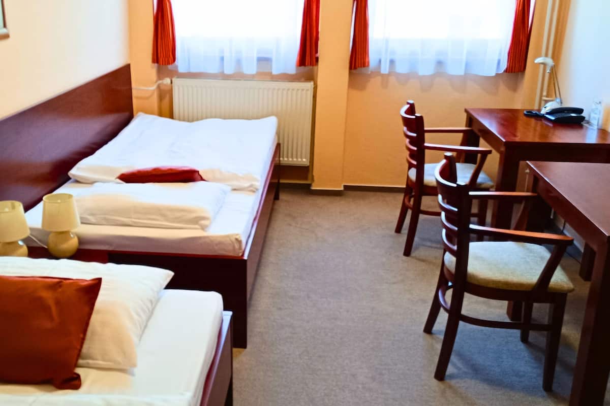 A hotel room with two single beds, a wooden desk, a chair, and a radiator.