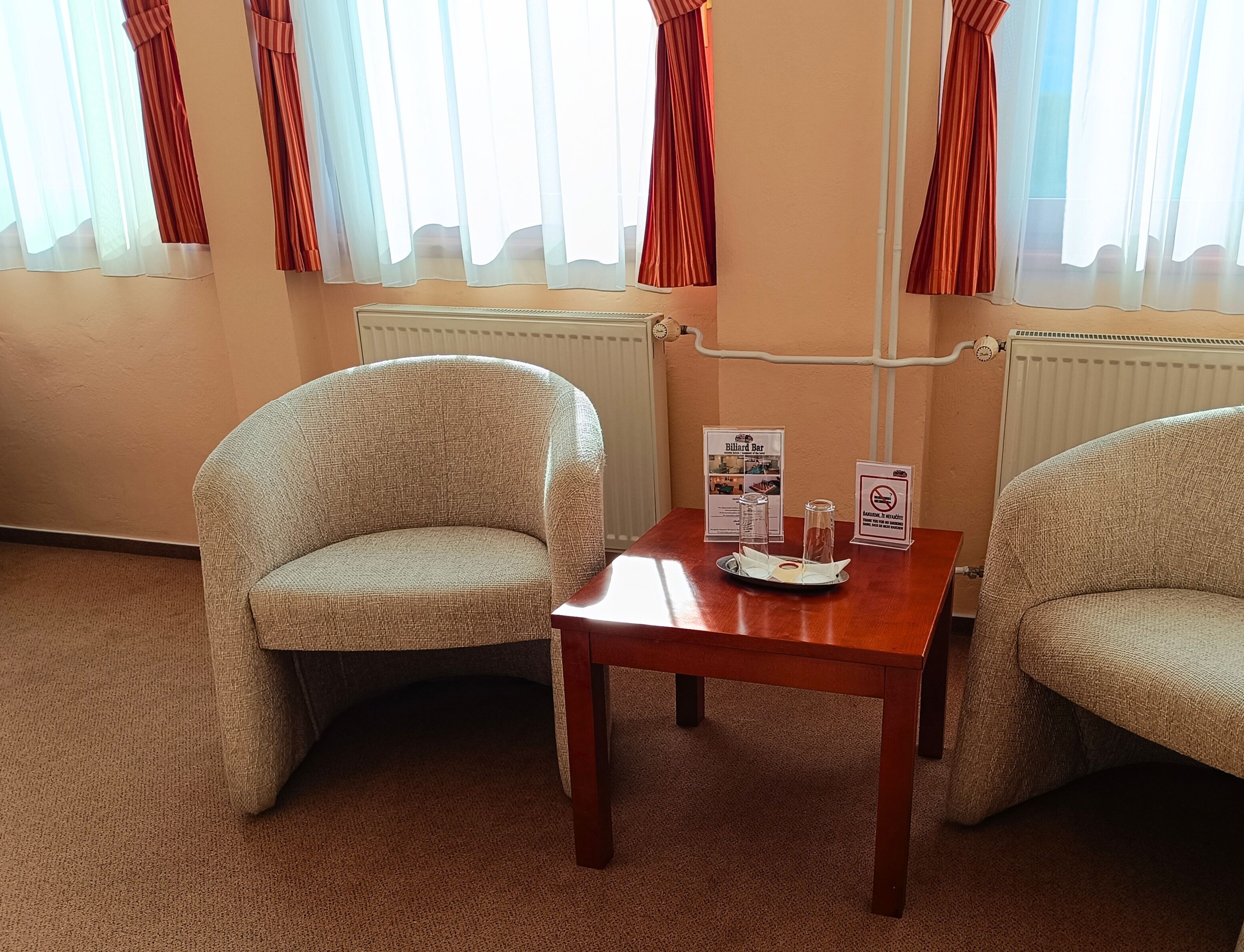 Una habitación con dos sillones, una mesa de madera con una bandeja de vasos y un cartel para bar de billar.
