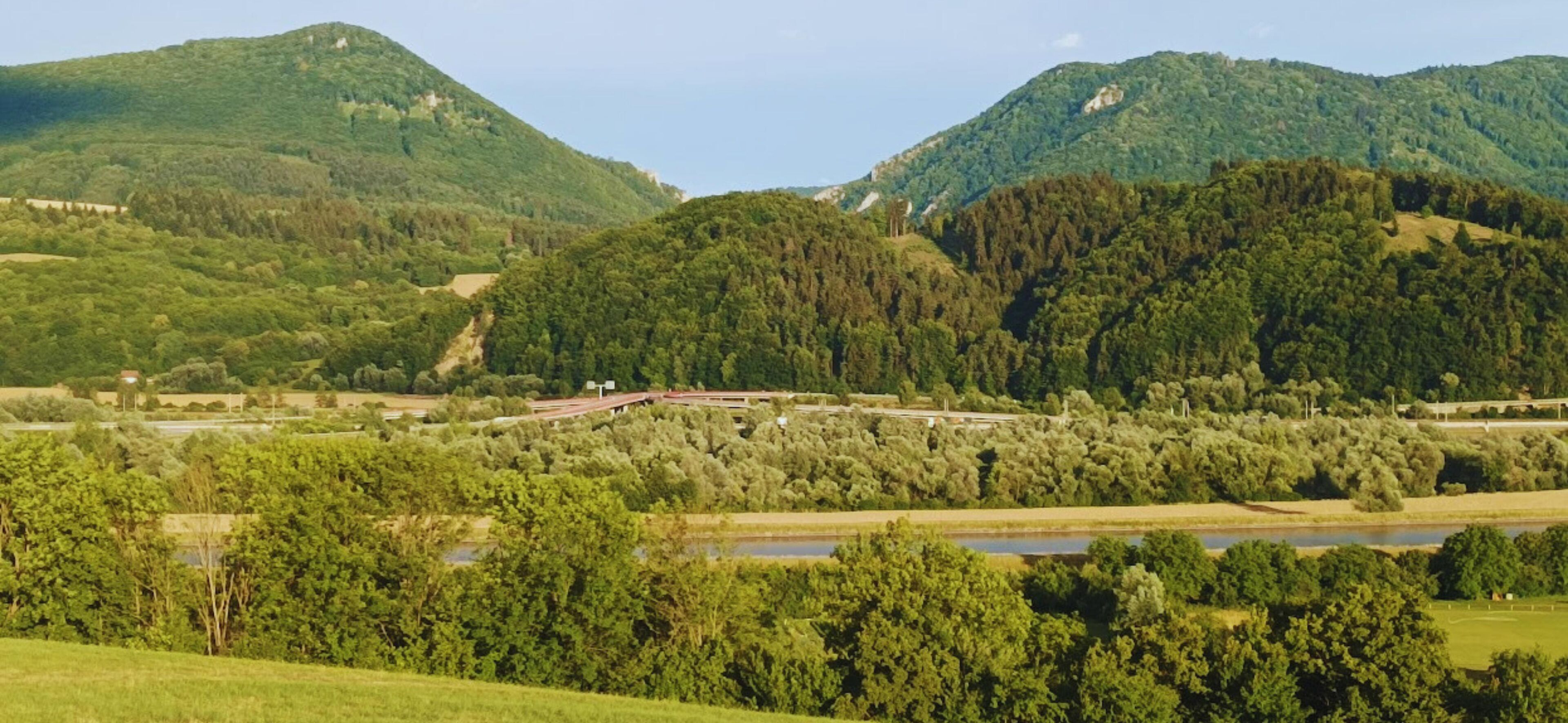 A rural landscape with rolling hills, a river, and a bridge.