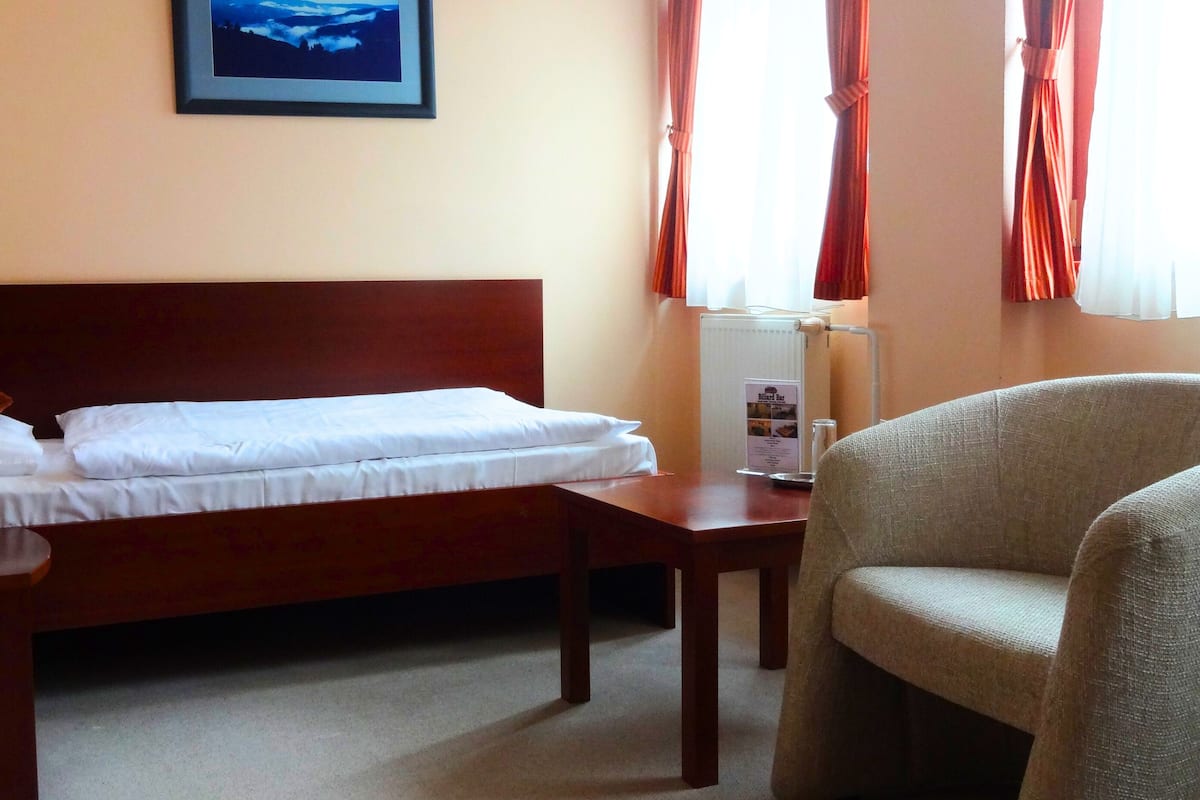 A hotel room with a bed, a chair, a table, a lamp, and a framed picture on the wall.