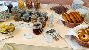 Una mesa de buffet con diversos alimentos y condimentos, incluyendo frascos de conservas, pan y pasteles.