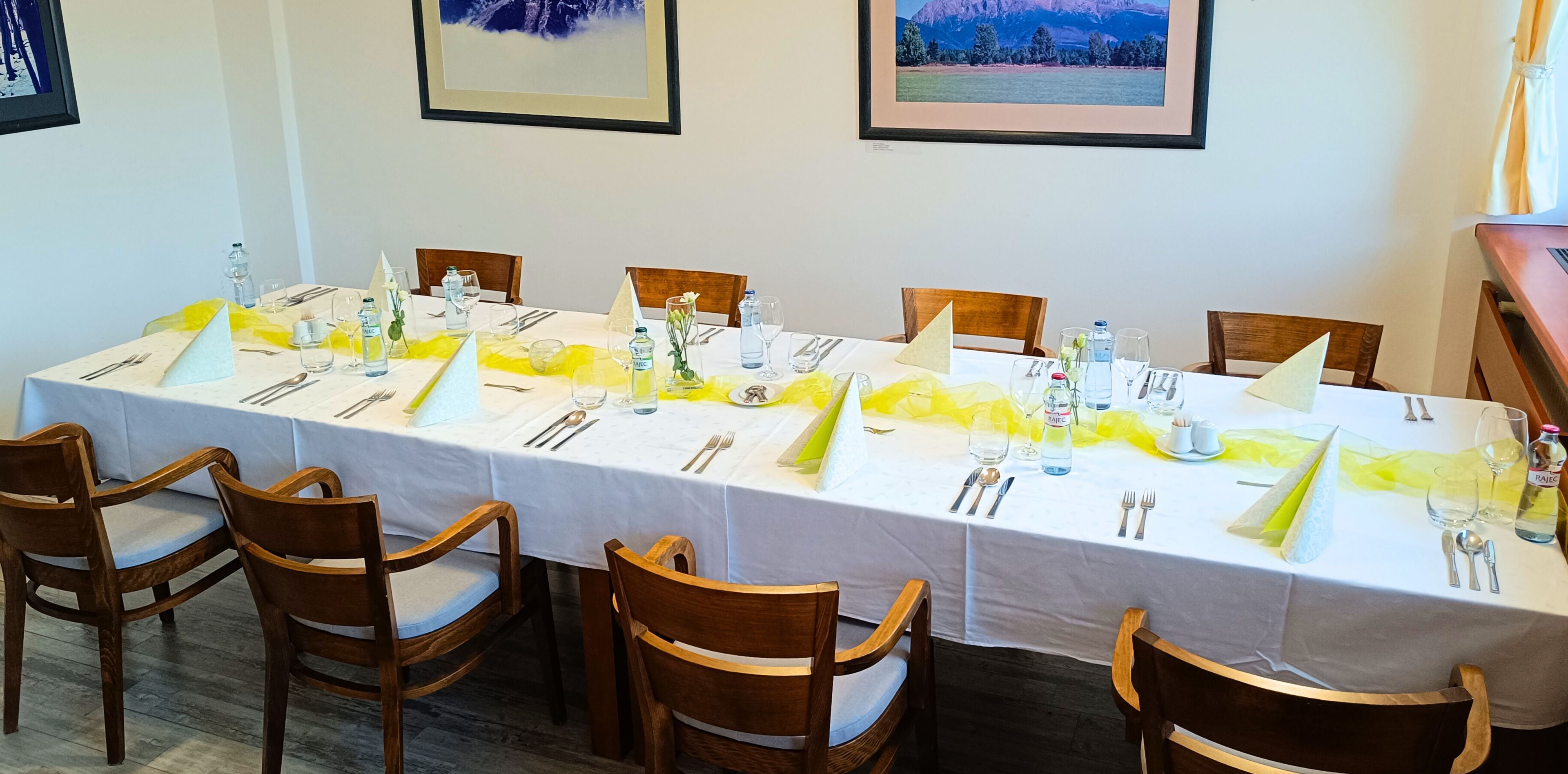 A dining area with a long table set for six, wooden chairs, and framed pictures on the walls.
