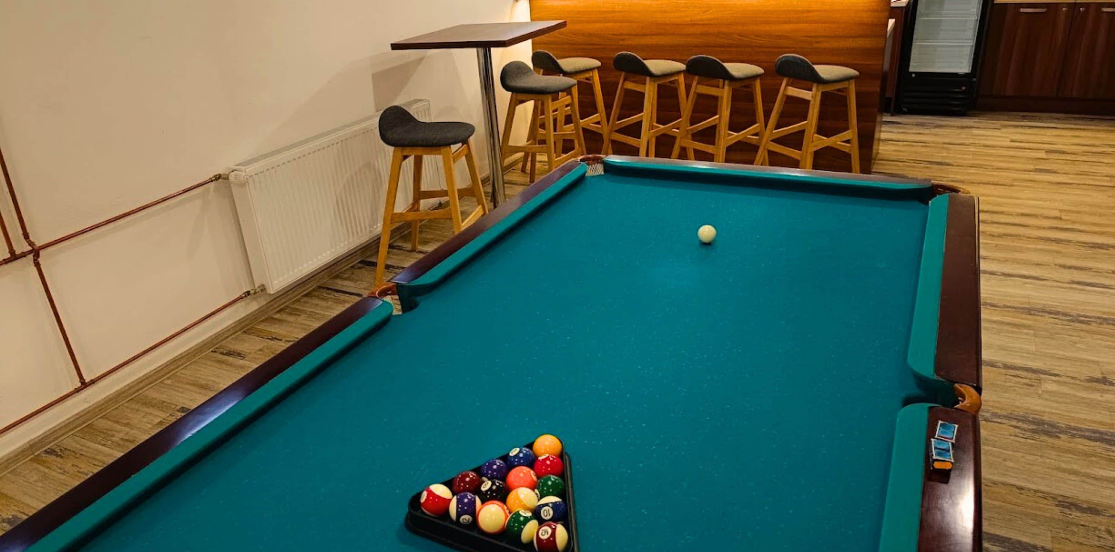 A billiard table with a set of stools and a bar area in a hotel room.