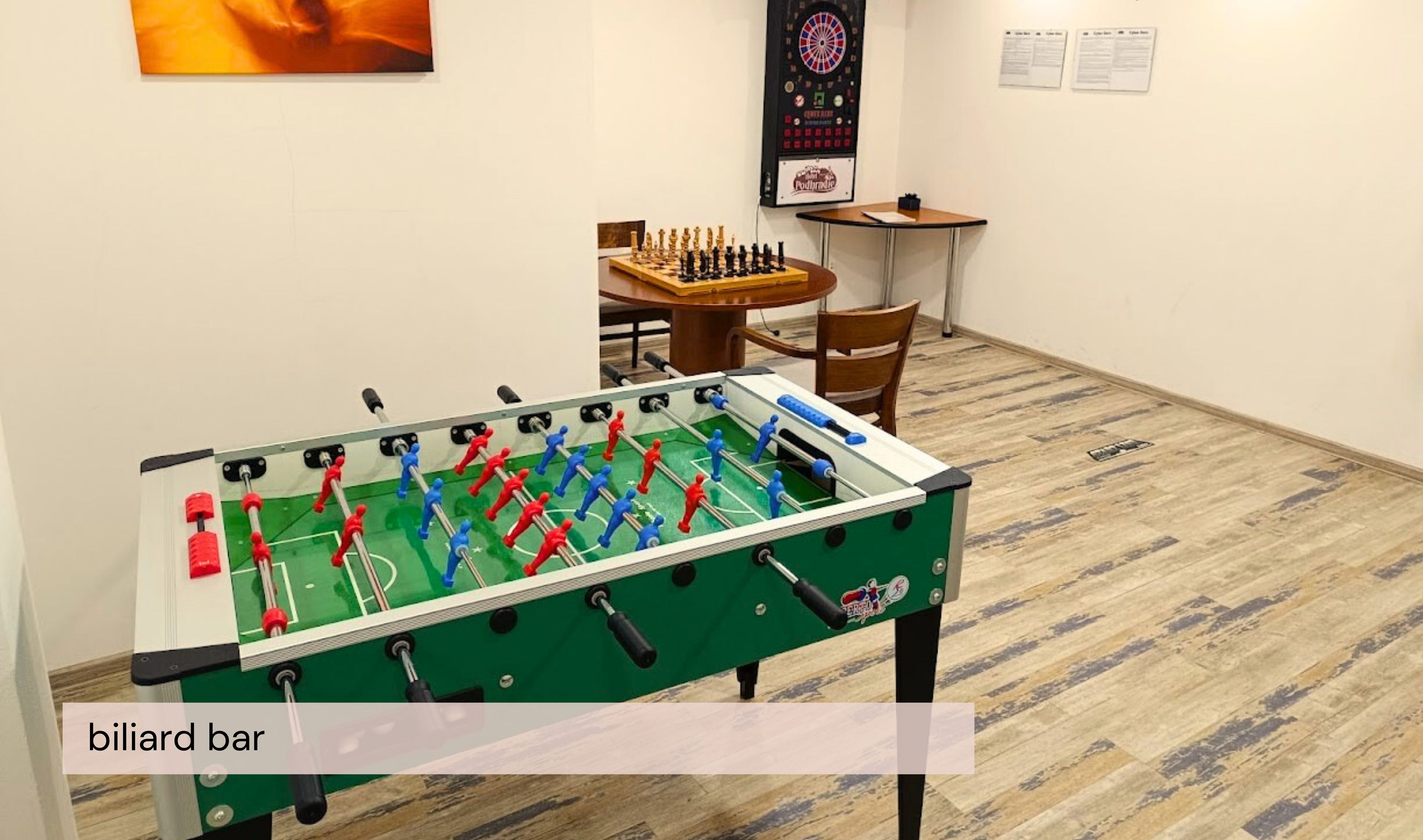 Una mesa de billar con la leyenda 'billar bar' en una habitación de hotel, junto a una mesa de fútbol de mesa, un dardo y un tablero de ajedrez.