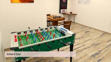 Una mesa de billar con la leyenda 'billar bar' en una habitación de hotel, junto a una mesa de fútbol de mesa, un dardo y un tablero de ajedrez.