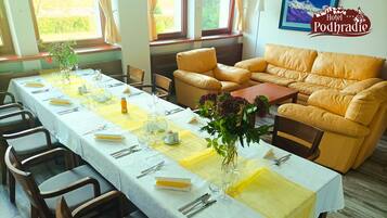 A long dining table set with yellow tablecloths, white tablecloths, and a vase of flowers. There is a sofa and a lamp in the background.
