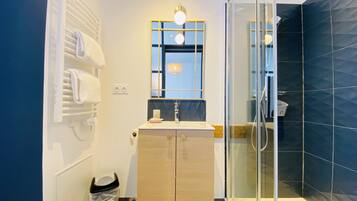 A modern bathroom with a glass shower enclosure, a white toilet, a beige vanity with a mirror, and a patterned floor.