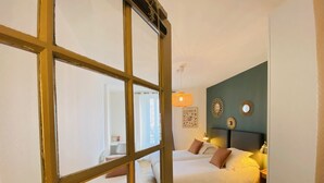 A bedroom with two beds, a wooden floor, and a view through a window with a yellow frame. - Hôtel Saint-Michel (Dinard)