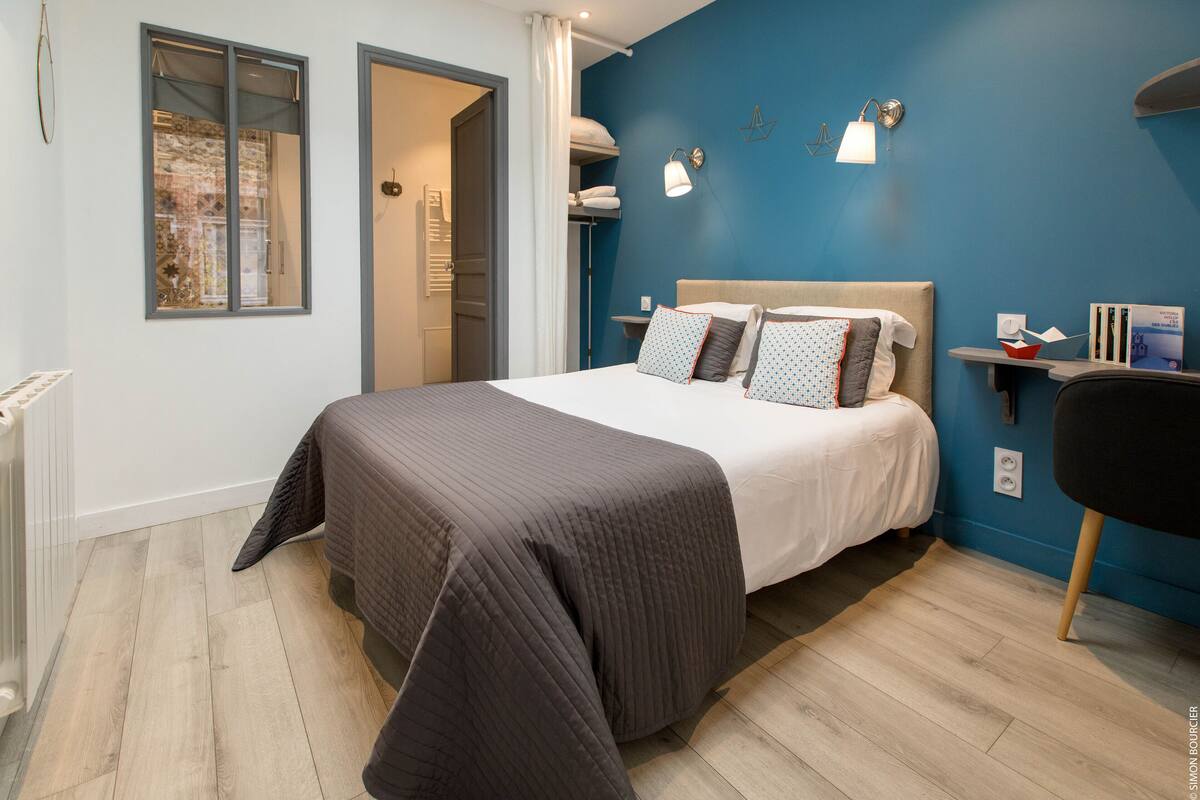 A modern hotel room with a large bed, a desk, and a blue accent wall.