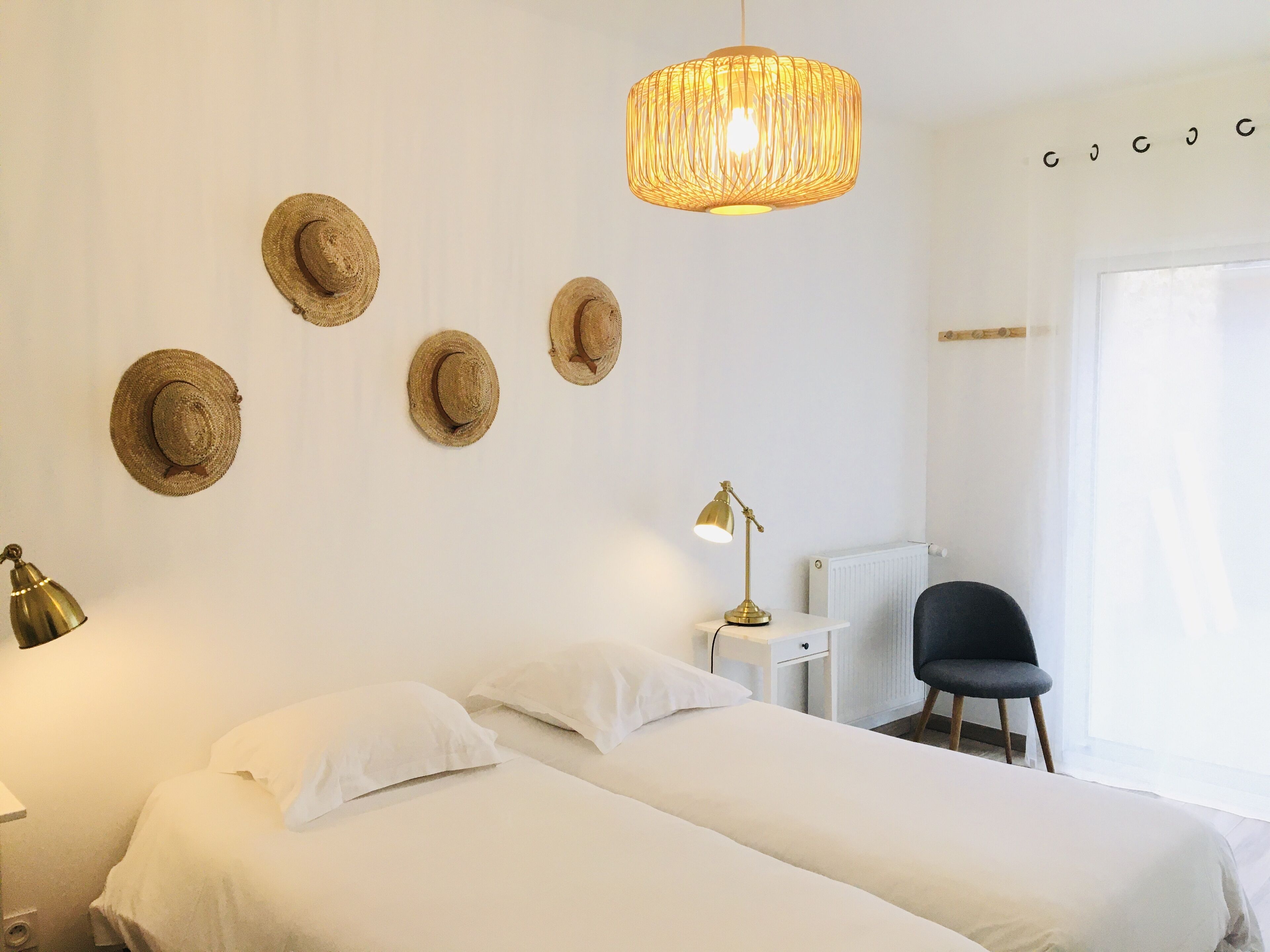 A bedroom with two beds, a desk, a chair, a radiator, and a hanging light fixture.