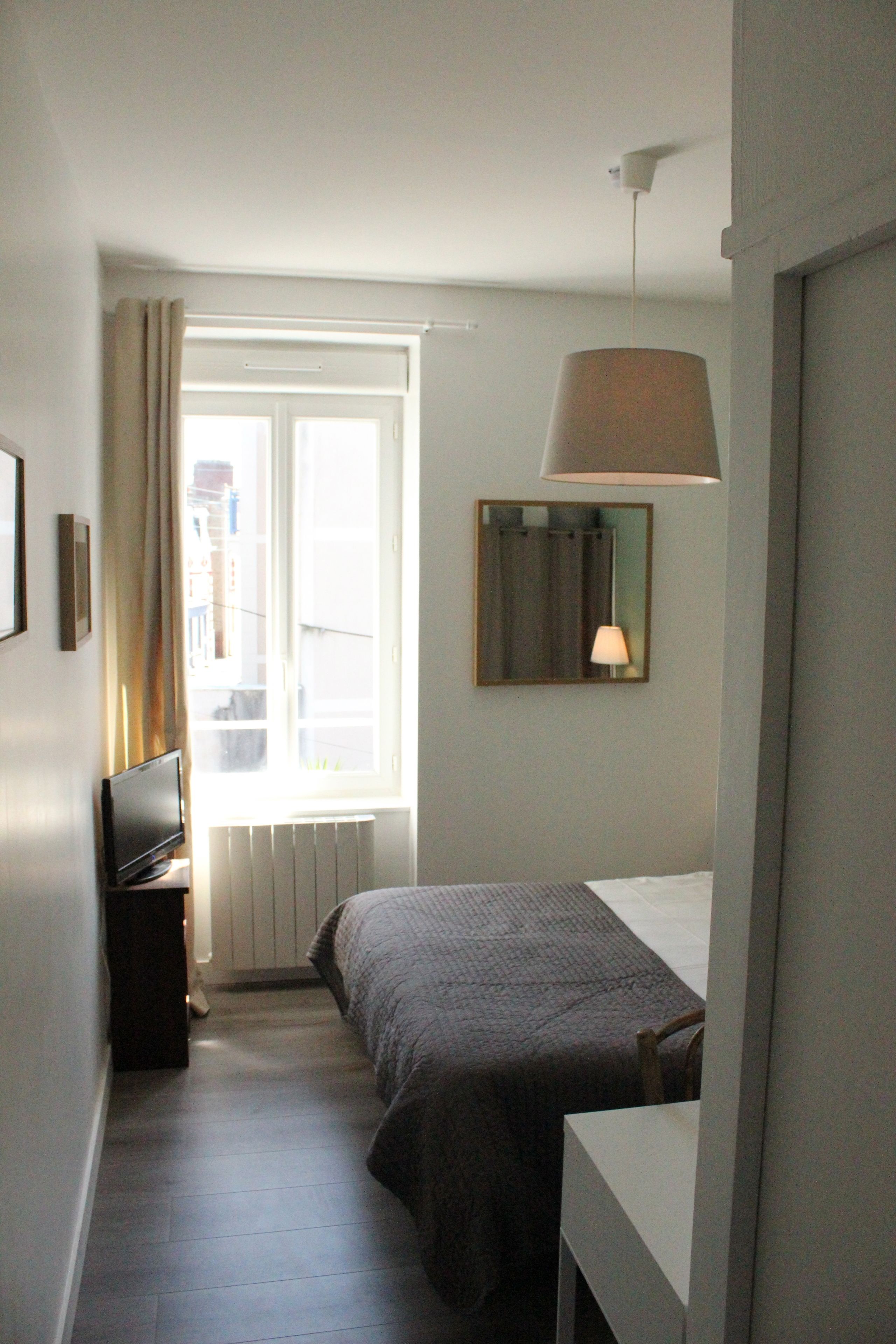 Een hotelkamer met een bed, een televisie, een lamp en een raam met gordijnen.