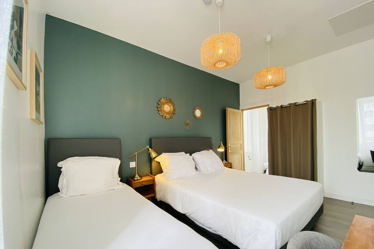 A hotel room with two beds, a wooden nightstand, a desk, and a window with curtains.