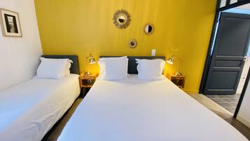 Une chambre d’hôtel avec deux lits, chacun agrémenté de draps blancs et d’oreillers assortis. On y trouve des tables de chevet avec des lampes, un miroir et un luminaire fixé au mur.