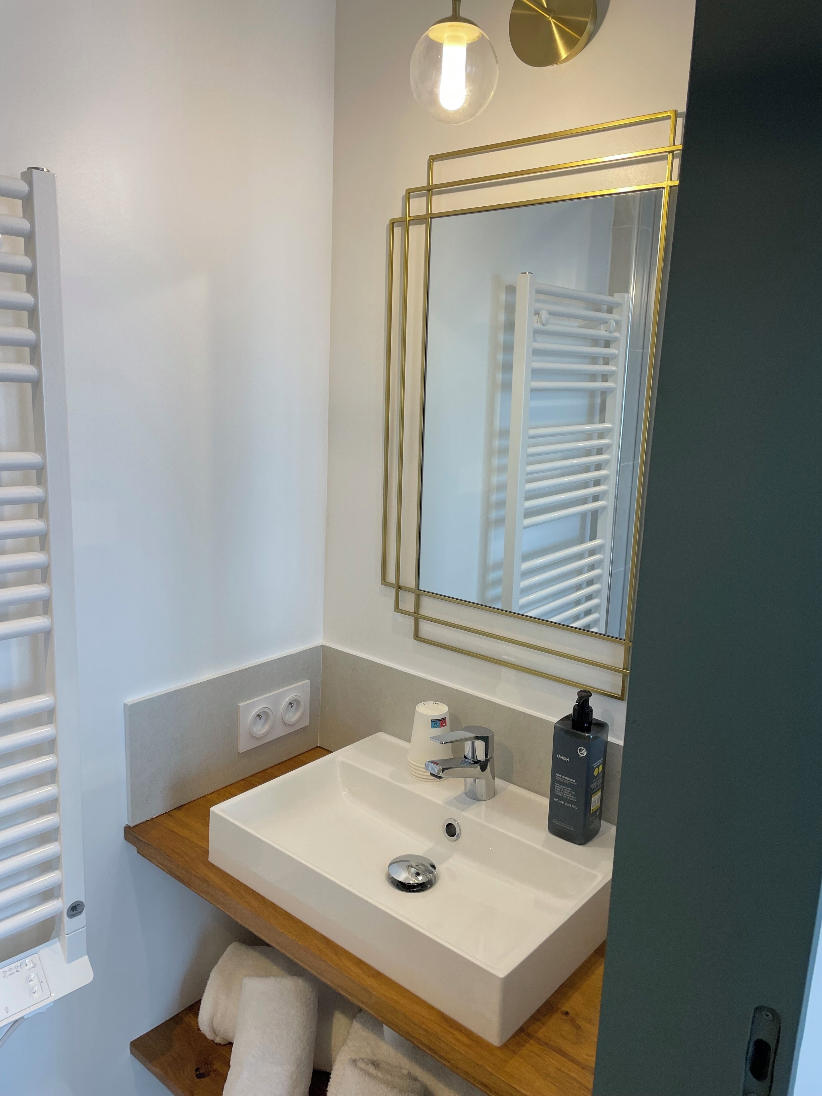 A modern bathroom with a white sink, a mirror with a gold frame, and a towel rack.