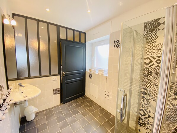 A bathroom with a black door, a white sink, a glass shower enclosure, and patterned tiles. - Hôtel Saint-Michel (Dinard)