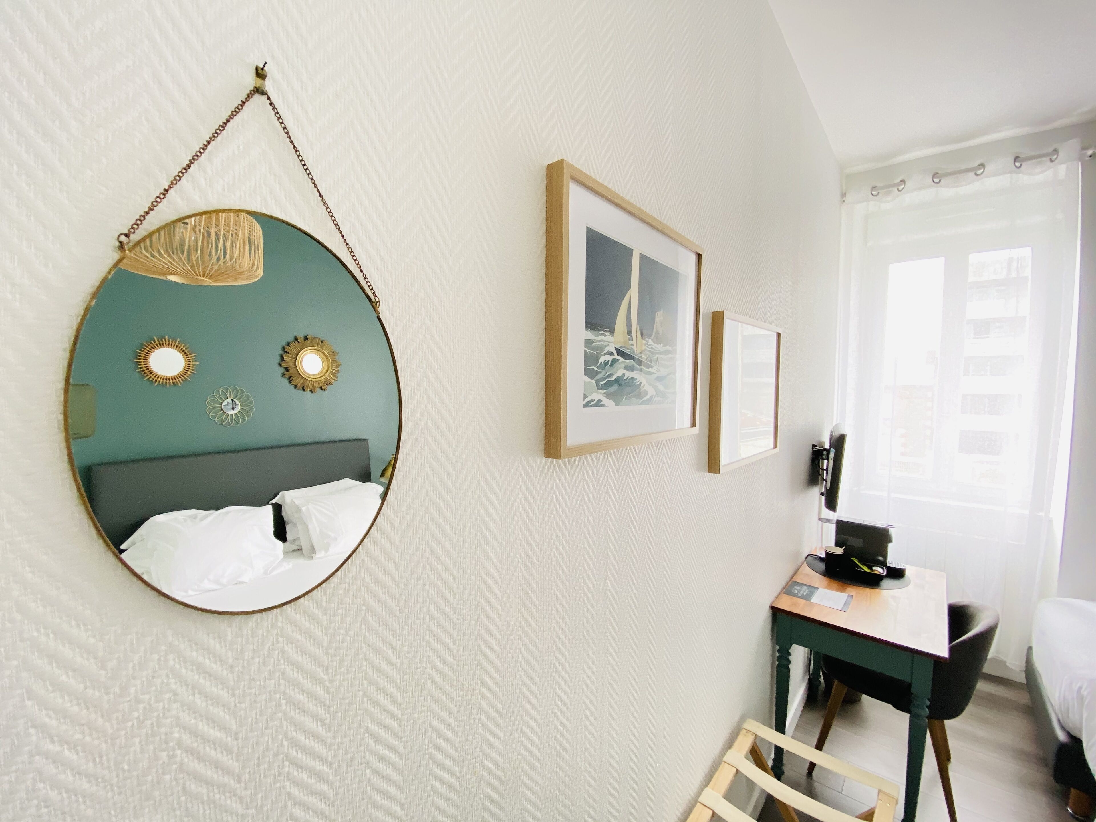 A hotel room with a bed, a desk, a chair, a mirror, and two framed pictures on the wall.
