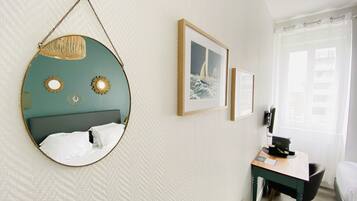 Une chambre d’hôtel avec un lit, un bureau, une chaise, un miroir et deux tableaux encadrés au mur.
